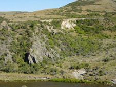 Broken formation (sheared greywacke; left) at Fiddlers Flat in the Manuherikia River gorge. White rocks in upper centre are Miocene sediments of the historical alluvial gold mine, and clay-altered greywacke immediately beneath the sediments. The boundary between sediments and basement (unconformity) dips gently to the right, and this zone contained the most abundant alluvial gold.