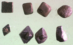 Grains of pyrite (FeS<sub>2</sub>, top row) and arsenopyrite (FeAsS, bottom row) from young (12000 years old) alluvial gold-bearing sediments at Macraes Flat. The largest grains are about 2 mm across. These gold-bearing sulphide minerals were eroded from unoxidised basement schist exposed when recent movement on the Macraes Fault offset the oxidized zone beneath the Waipounamu Erosion Surface. The grains on the left have been little affected by sedimentary transport, and still have their sharp crystal shapes. The grains on the right have been partially rounded by transport.