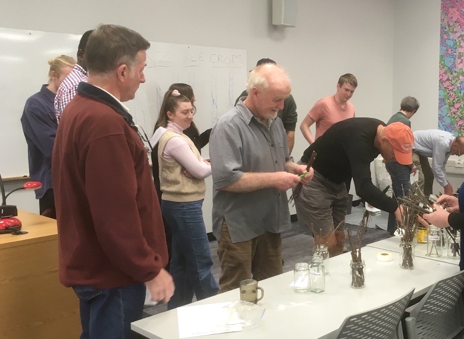 Small group of people watch a man manipulate twigs.