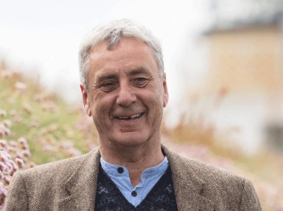 A head and shoulders of a man with flowers behind him