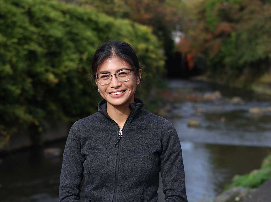 A woman standing in front of a river and greenery