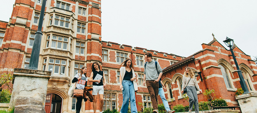 Students walking in front of Knox College, a historic red-brick building, carrying books and backpacks.