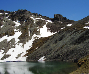 An alpine tarn surrounded by snow capped schist.