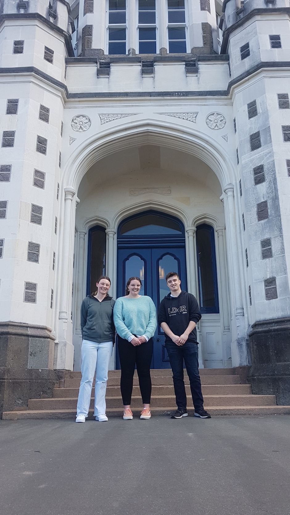Three students standing outside an old stone school building.
