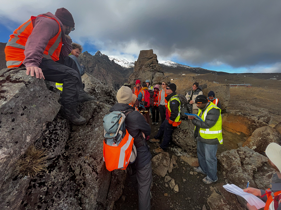 A group of people in hi-vis vests gathered in a rocky, mountainous area