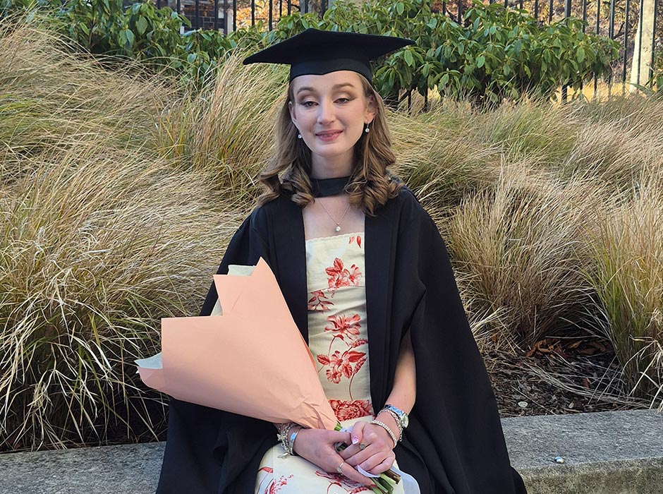 A female graduate in regalia, holding a flower bouquet