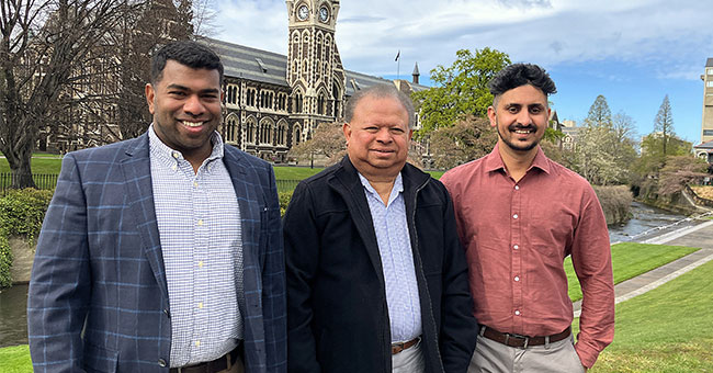 Three men are pictured with the University Clocktower in the background.