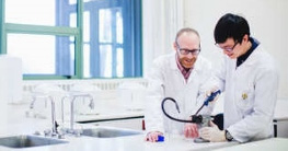 Two people in lab coats and goggles working in a laboratory image