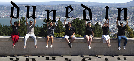 Students sitting on a wall holding up letters that spell Dunedin