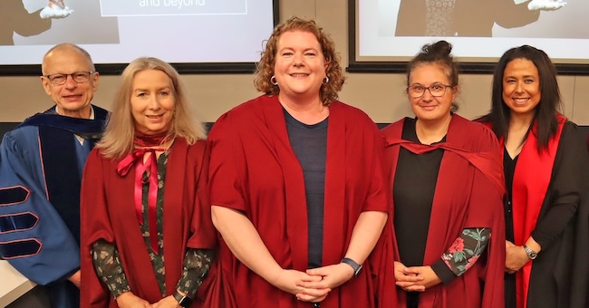 Five people dressed in academic regalia smile at the camera.