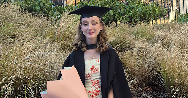 A female graduate in regalia, holding a flower bouquet