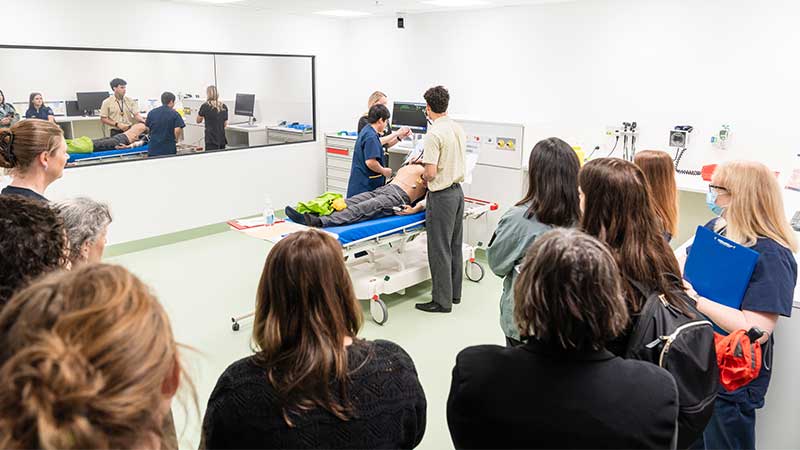 Two people standing around a bed with a crowd of people observing