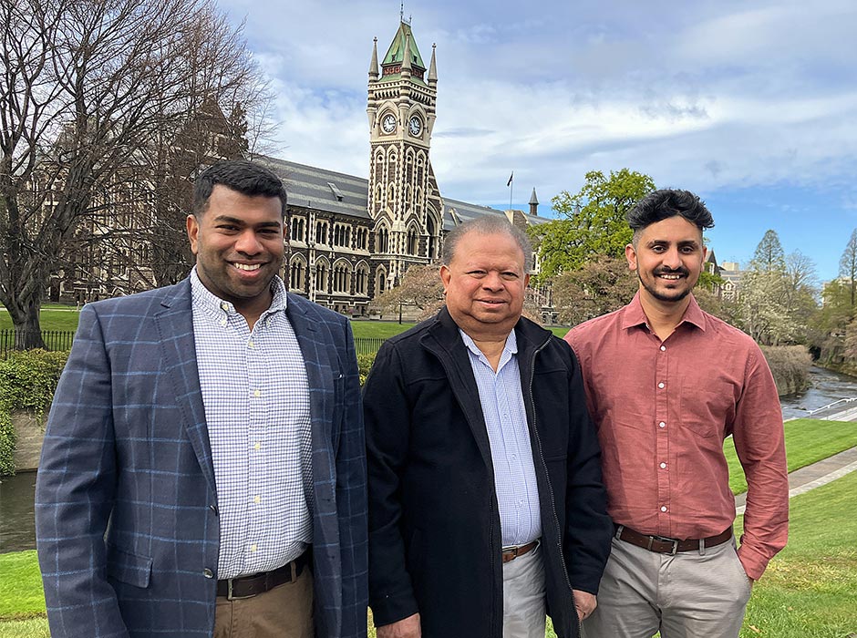 Three men are pictured with the University Clocktower in the background.