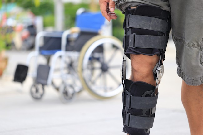 Close-up of a man's knee in a stabiliser support brace, with a wheelchair in the background