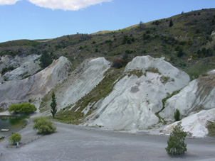 Clay-altered greywacke (white, centre and right) at the Miocene unconformity beneath gold-bearing quartz gravels (left) at Blue Lake, St Bathans The Miocene unconformity and quartz gravels dip ~30° to left.