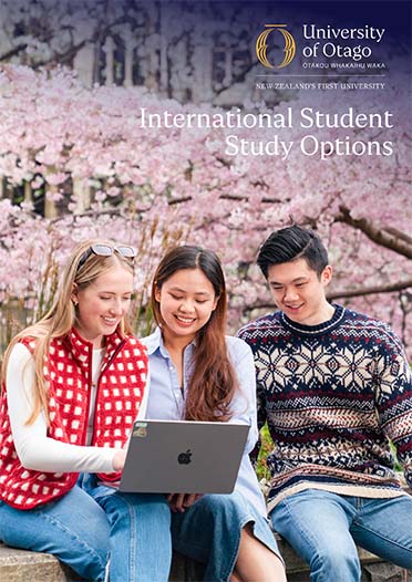 Cover image of three students looking at a laptop in front of a blossom tree