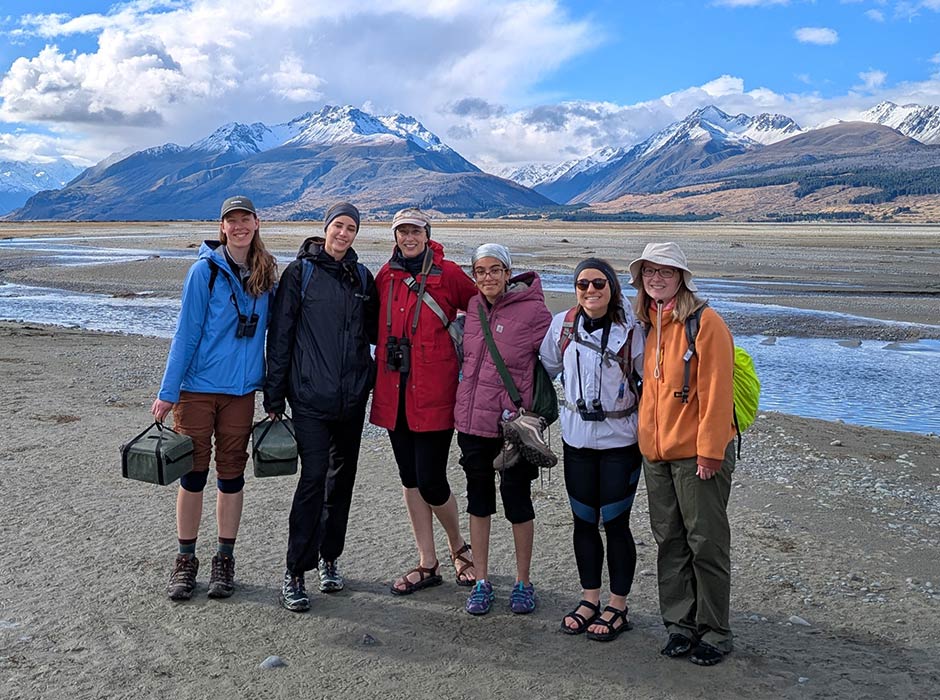 six women standing in front of a river with mountains in the background 