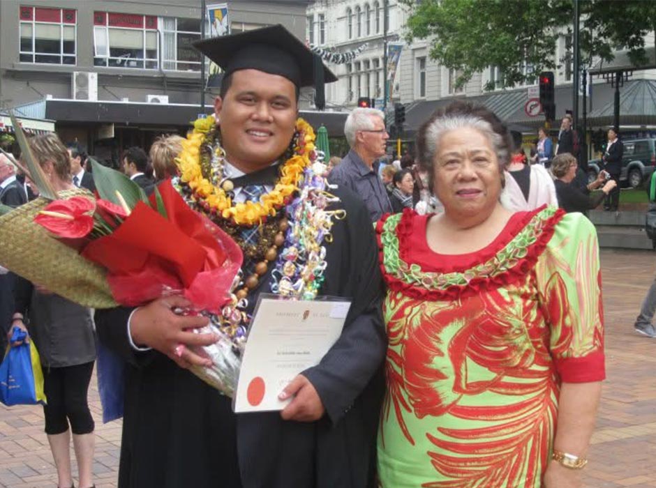 A man dressed for graduation poses for a photo with an older woman.