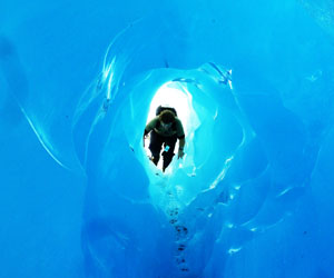 Hiking through a meltwater cave, created the previous night during heavy rainfall, inside the temperate Franz Josef Glacier; Fiordland, New Zealand