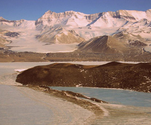 The Koettlitz Glacier peels around Heald Island as it flows toward McMurdo Sound. The Walcott Glacier flows through the Royal Society Range in the background.