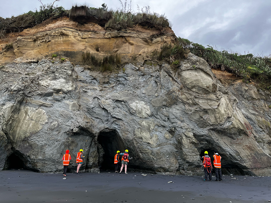 A group of people in hi-vis vests and hard hats at the base of a cliff