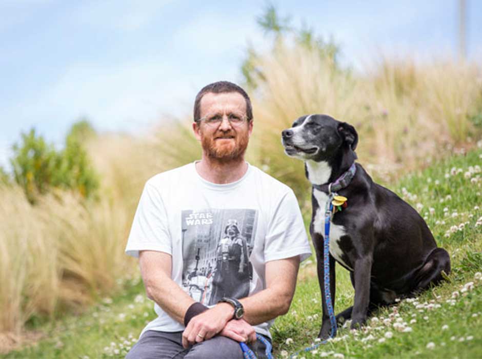 A man sitting on grass with his black dog 