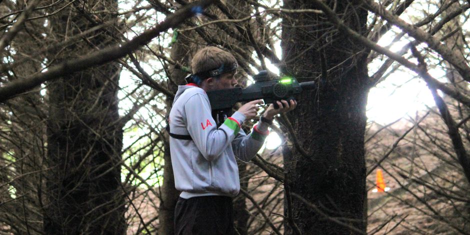 A person aiming a laser tag gun in a forest of bare trees.