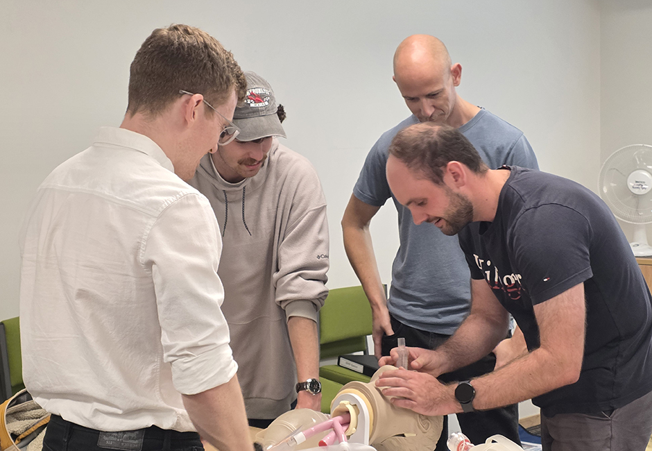 Four male students practise inserting a ventilation breating tube into a plastic mannequin.