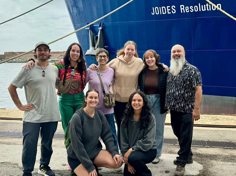 A group of people pose in front of a boat.
