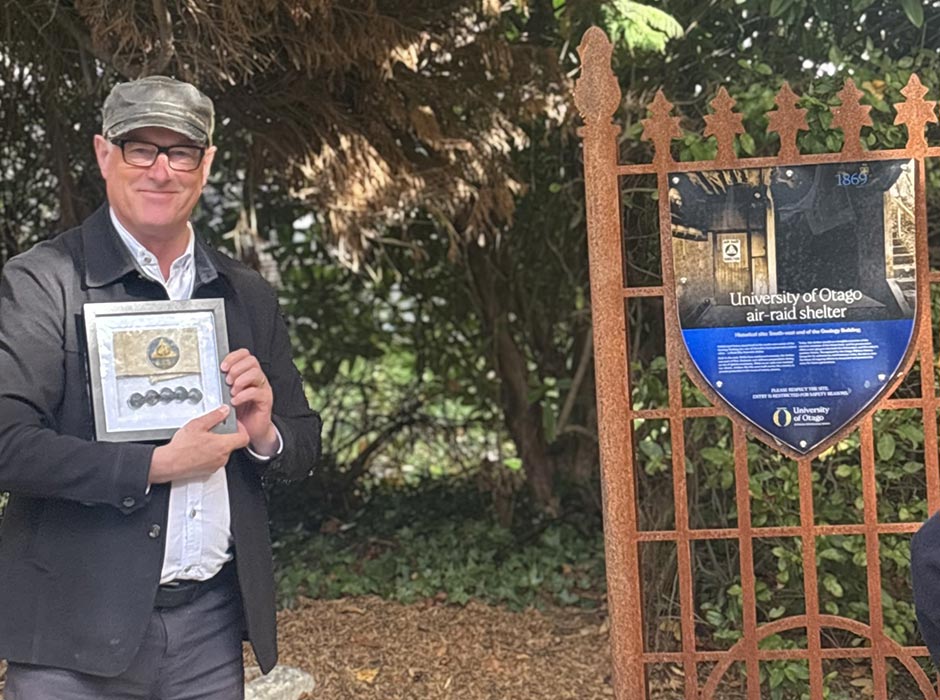 A man holding war memorabilia standing nest to a sign for an air raid shelterr 