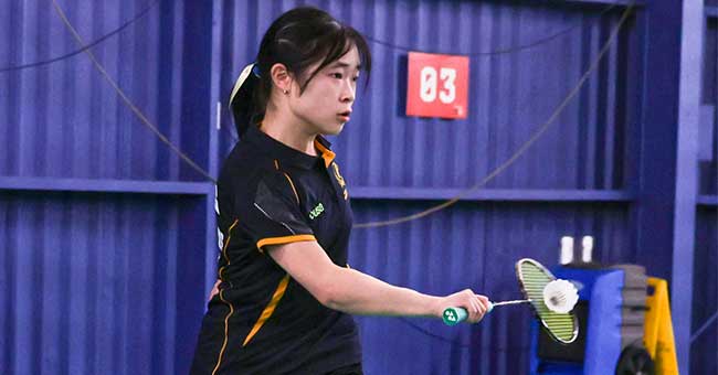 A woman from the waist up holding a badminton racket about to hit a shuttlecock