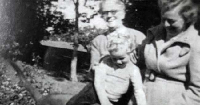 A black and white image of a young girl sitting on top of a dog with a lady standing behind them and another lady standing next to them