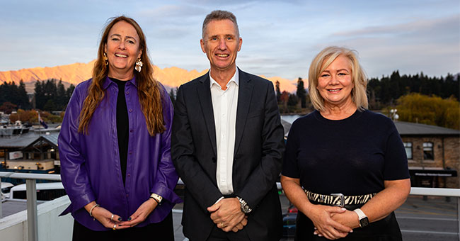 Three people pose for a photo against a Queenstown backdrop.