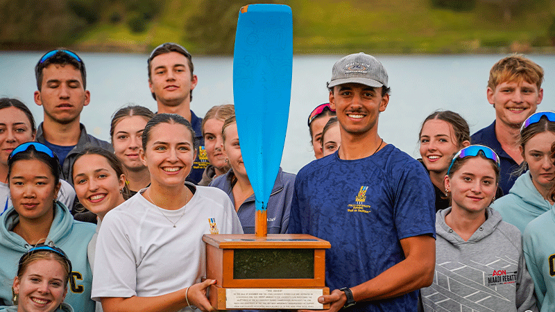 Two people holding a trophy, with team mates around them
