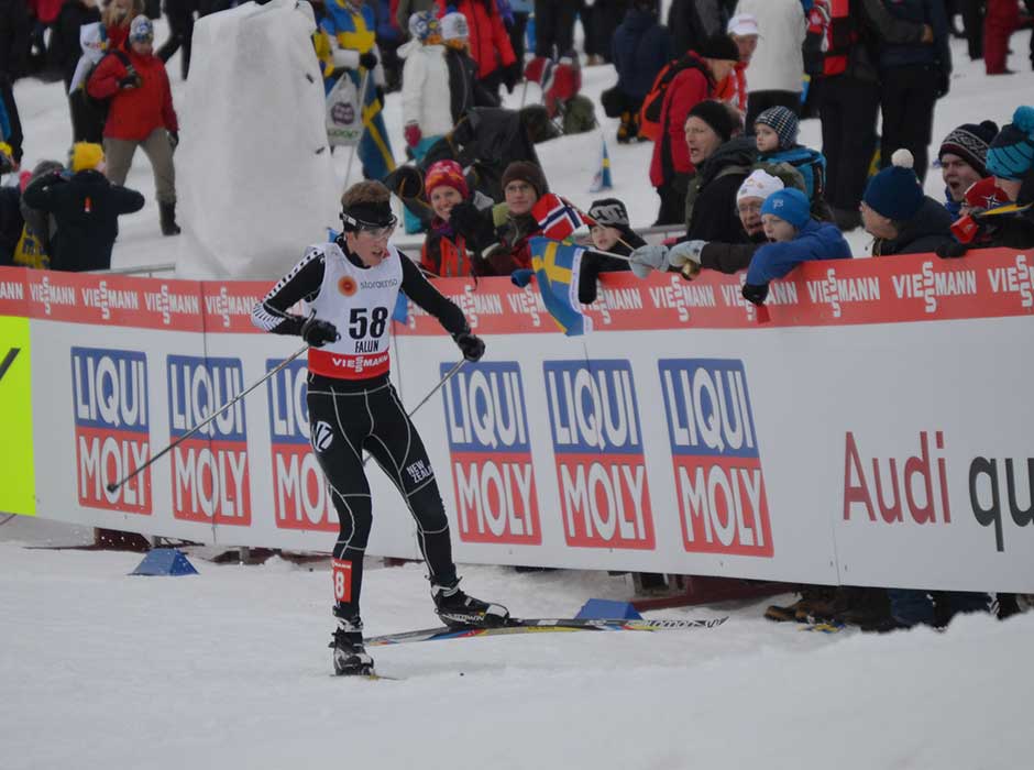 A man on skis and snow going past a crowd of people