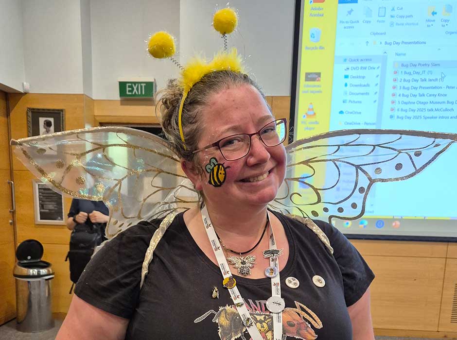 A woman wearing a black t shirts with fairy wings and bumble bee antennae on her head 