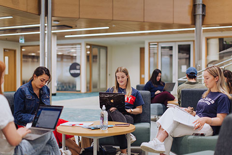 Four students sitting on the grass and studying in front of Otago clocktower