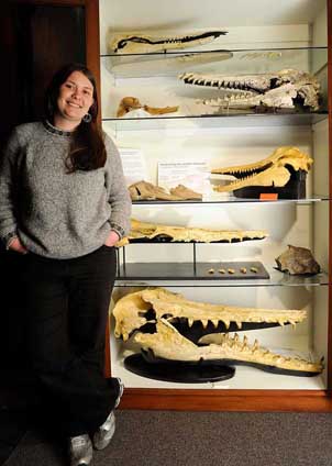Dr Carolina Loch (Otago PhD on form and function of cetacean teeth) next to a display case that contains skulls of toothed fossil cetaceans from New Zealand. Specimens include a kekenodontid archaeocete, squalodontids, and putative archaic platanistoids
