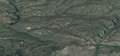 Oblique view of Tucker Hill from the northwest, with Manuherikia River, rail trail, and town of Alexandra in the foreground. The rugged topography results from uplift of schist bedrock along faults that have been active periodically for 100 million years. A white scar at centre left (near the Lower Manorburn Dam) is a remnant of 20 million year old sediments that have been uplifted and tilted along a fault zone.
