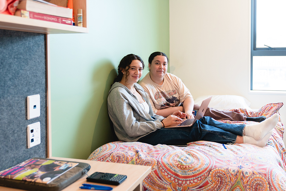 Two students sitting on bed in bedroom