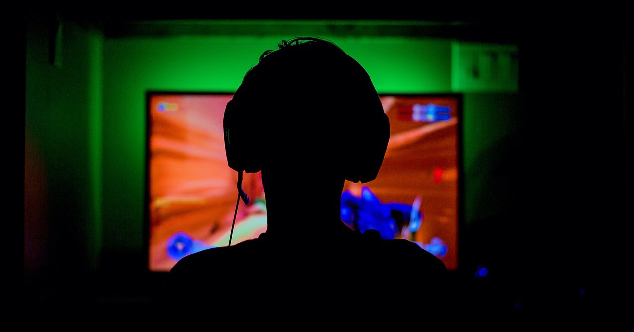 Silhouette of a computer gamer in a dark room, sitting in front of a monitor.