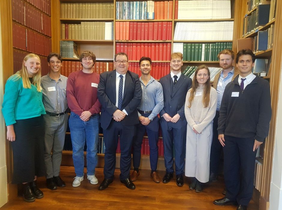 A row of people standing in front of a book case 