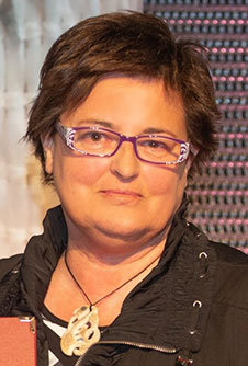 head and shoulders of a woman with short dark hair, glasses, wearing a bone carving around her neck 