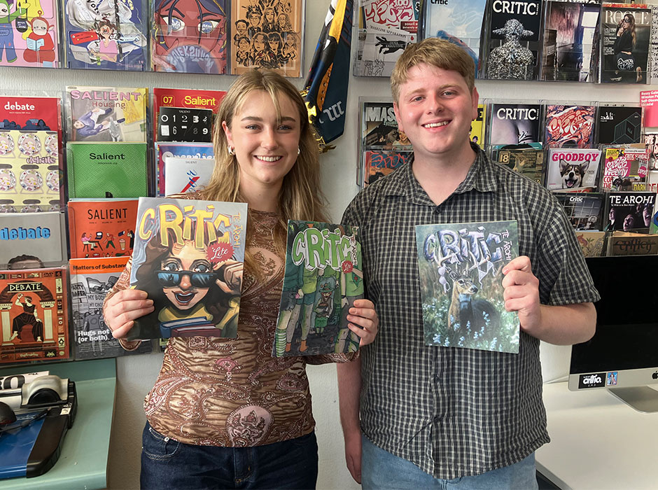 A woman and a man standing next to each other, each holding up a copy of Critic magazine, with many magazines on the wall behind them