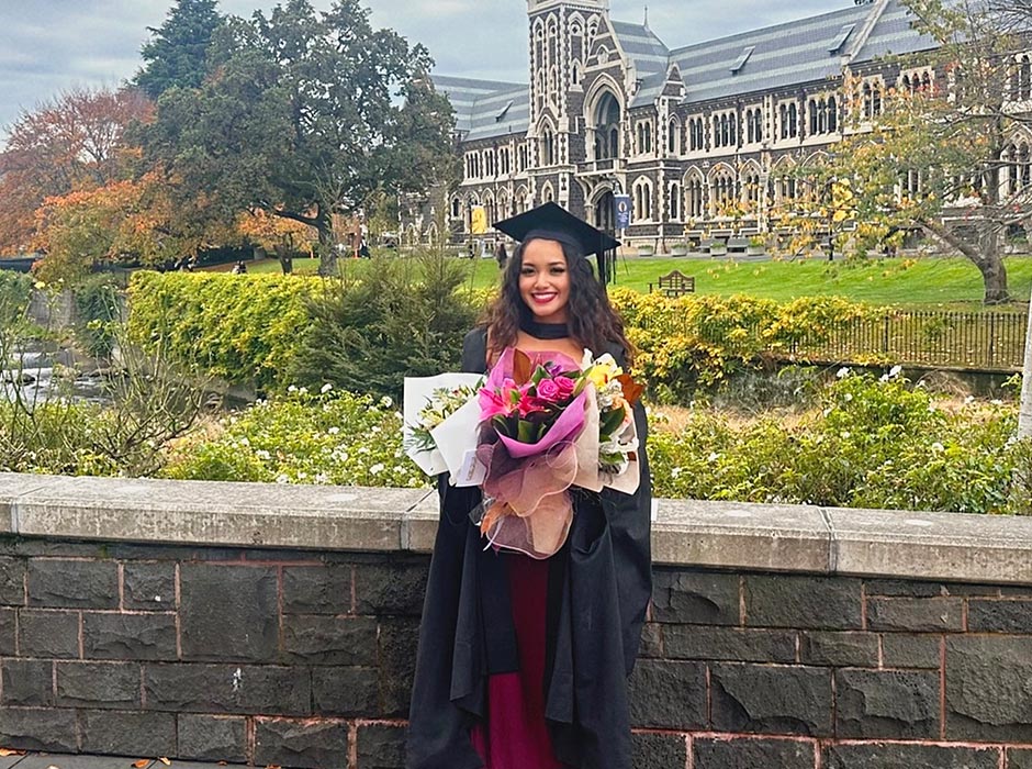 A woman dressed in graduation robes is pictured in front of the Clocktower.