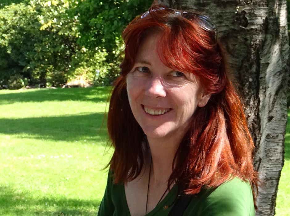 A woman with red hair is pictured at a picnic table in a park.