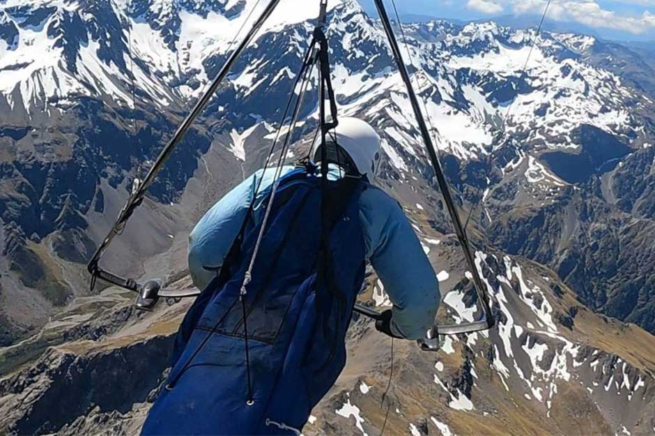 A person hang gliding over some snow-capped mountains on a sunny day