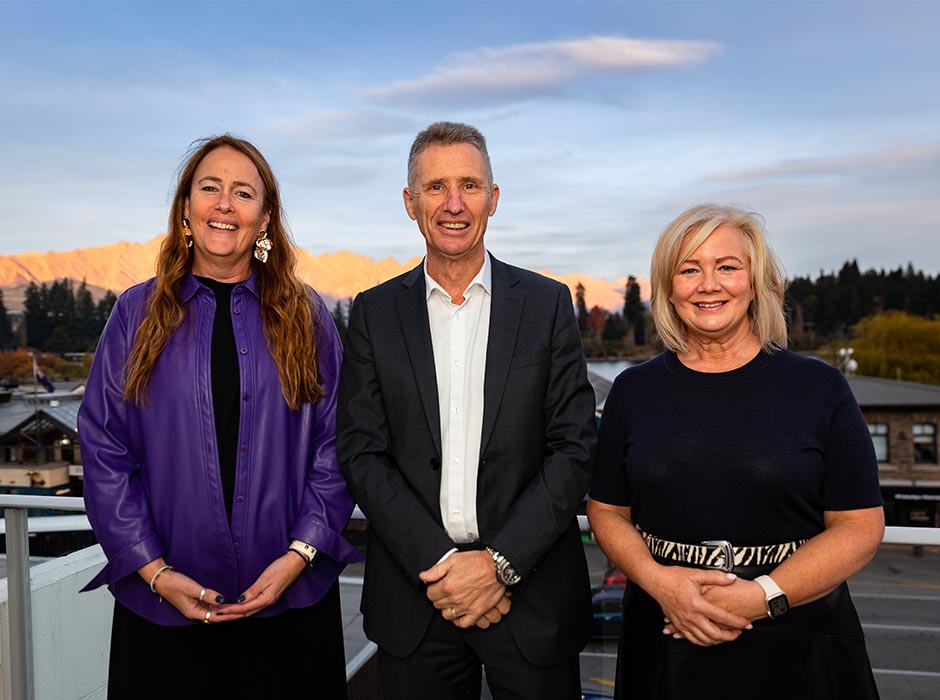 Three people pose for a photo against a Queenstown backdrop.
