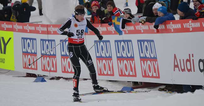 A man on skis and snow going past a crowd of people