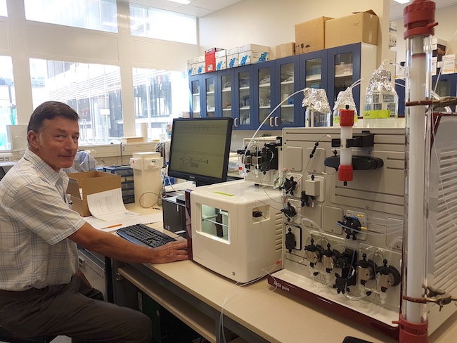 Associate Professor Alan Carne sitting in front of a computer and some chromatography equipment in his lab.